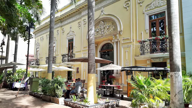 Yellow colonial building with intricate carvings and palm trees in front in Merida, Mexico