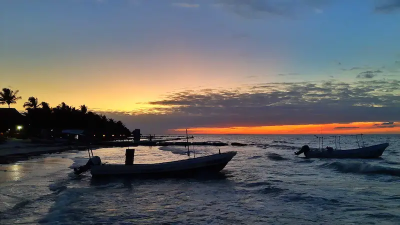 Fishing boats and palm trees in bright orange sunset on Isla Holbox, Mexico