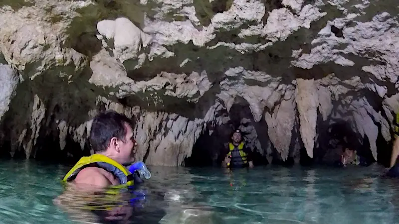 Man swimming through clear water surrounded by rocks in cave cenote Sac Actun in Tulum, Mexico