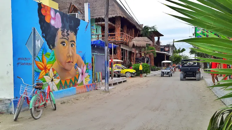 Sandy street with colourful wall mural, bikes and golf carts in Isla Holbox, Mexico.
