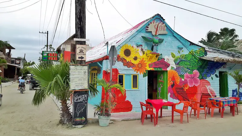 Restaurant covered in bright graffiti with plastic furniture on sandy street on Isla Holbox, Mexico