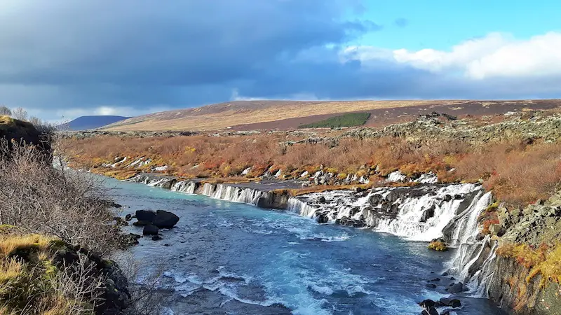 low waterfall, Hraunfossar, with water cascading through a lava field into the side of a river. Iceland.