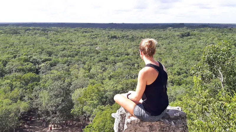 Girl sitting on top of a Maya pyramid looking over jungle at Coba, Mexico