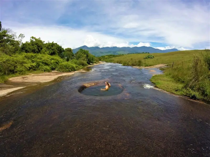 Woman sitting in a natural pool in a river surrounded by countryside and mountains in Guadalupe, Colombia.