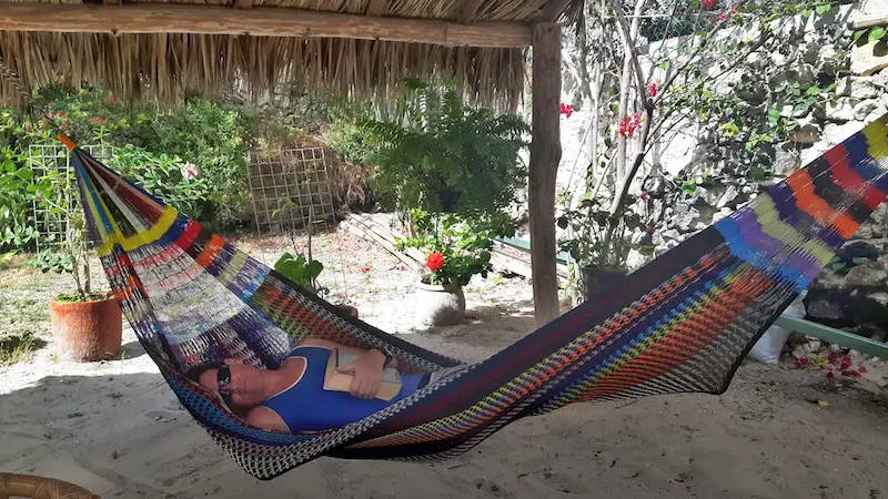 Man in a colourful hammock under a palapa roof with a sand floor in Progreso, Mexico house sitting.