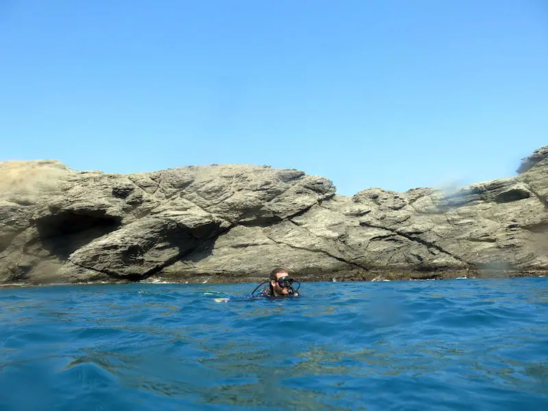 Man floating in the blue water with scuba gear on with rocks behind in Taganga, Colombia.