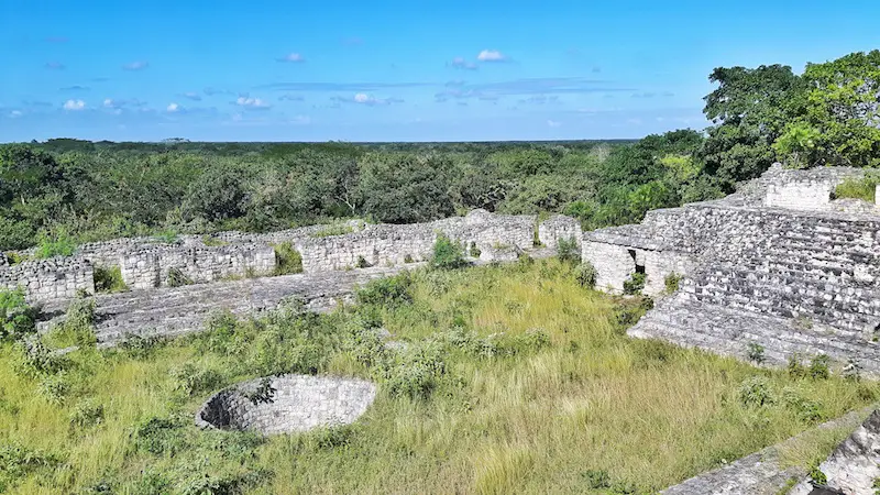 An ancient plaza filled with long grass and a stone well on the Acropolis at Ek Balam ruins, Mexico.