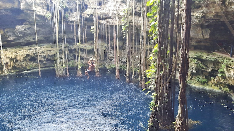 Man on a rope swing into Oxman Cenote, Mexico.