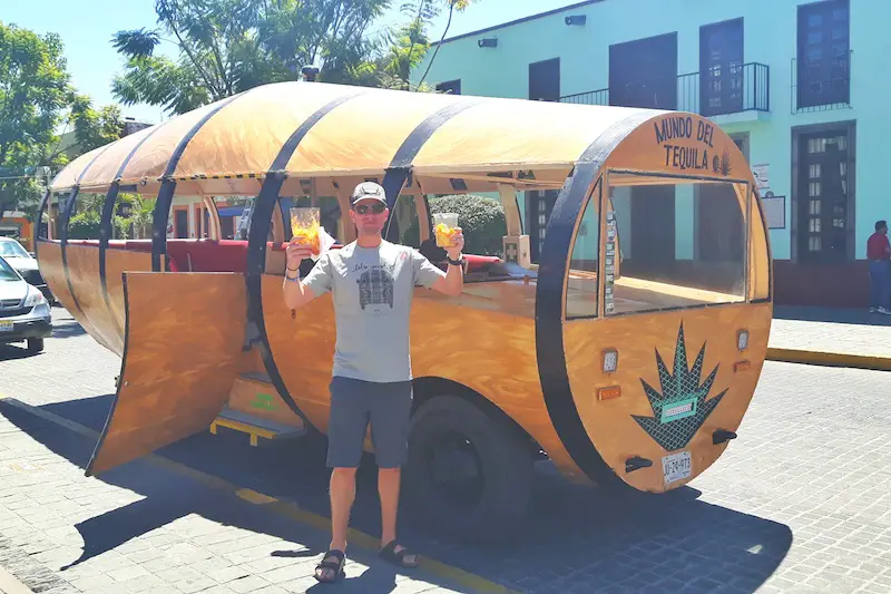 Man with snacks beside a car designed like a tequila barrel on a tequila tour, Jalisco Mexico.