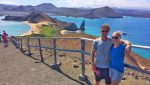 Man and woman in hiking gear with Pinnacle Rock behind in Galapagos Islands.