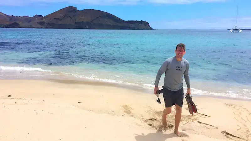 Man walking on a beach with snorkel equipment in his hands in the Galapagos Islands.