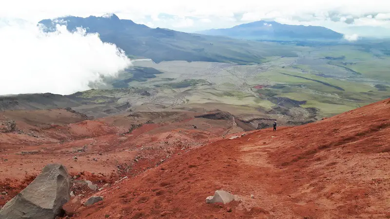 Red lava rock on Cotopaxi hiking trail with views beyond, Ecuador.