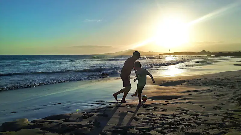 Man and boy playing soccer on Isla Isabela beach at sunset in Galapagos.